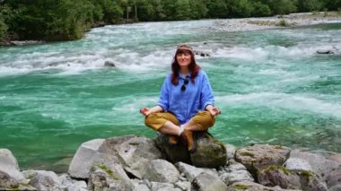 Kız büyük bir taşın üzerinde oturur ve bir dağ nehrinin yanındaki şelalenin yanında meditasyon yapar..