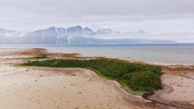 Issız kumsal sahili ile gök mavisi deniz suyu arasında Myrland Sahili, Flakstadoy, Lofoten Adaları, Norveç 'teki dağlara karşı hava hareketi.