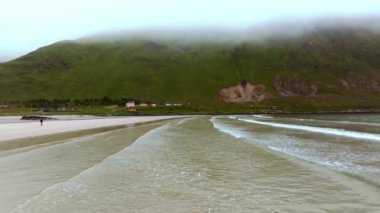 Dalgalar Haukland denen kumsalı yavaşça yıkıyor. Gün batımında çok sakin bir atmosfer ve arka planda karlı bir manzara ve dağlar. Çevre ışığı ve pozitif titreşim