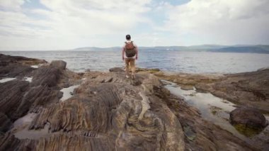 Sırt çantalı bir adam dağlardaki kumlu sahilde tek başına yürüyor. Norveç 'te yaz tatillerinde seyahat konsepti macerası yaşıyor.