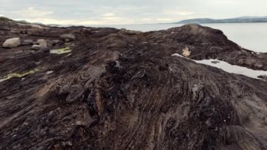 Bulutlu soğuk havada kara volkanik kayalık kıyıların havadan görünüşü. Vahşi doğayı keşfetmek, İzlanda ya da Norveç 'i gezmek