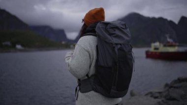 Tatiller. Yakından bakınca, kahverengi saçlı genç bir kadın sakin gölü ve ufuktaki dağları düşünüyor..