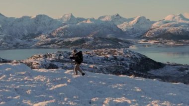 Sırt çantalı bir yürüyüşçü dağın tepesine tırmanıyor, dağcılık konsepti. Karda yürüyen, kışın yürüyüşe çıkan bir adam. Macera gezisi, doğa konseptindeki insanlar. Günbatımı destansı kar manzaralı dağ manzarası