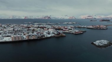 Norveç 'in Lofoten Adaları' ndaki Henningsvaer balıkçı köyünün kışın gün batımında hava manzarası. Kardaki dağlar, deniz, kayıklar, köprü, yol, bulutlu gökyüzü, kasaba, terör bürosu ve evler
