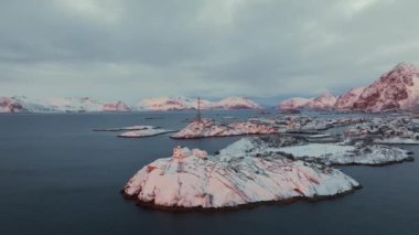 Norveç 'in Lofoten Adaları' ndaki Henningsvaer balıkçı köyünün kışın gün batımında hava manzarası. Kardaki dağlar, deniz, kayıklar, köprü, yol, bulutlu gökyüzü, kasaba, terör bürosu ve evler