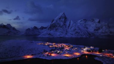 Deniz manzarası, karlı dağlar, kışın gün batımında daha kötü. Lofoten Adaları, Norveç. Fiyort, ev, sudaki yansıma, taşlar, kayalar, alacakaranlıktaki pembe bulutlu mavi gökyüzü. Göl