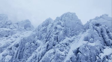 Engebeli, karla kaplı dağ zirvelerinin büyüleyici ve manzaralı manzarası güzel bulutlu bir atmosferin ortasına kurulmuş.