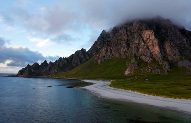 Sakin sahil ve kumlu sahille buluşan görkemli dağları gösteren nefes kesici panoramik bir manzara.