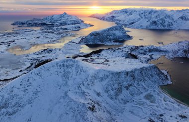Nefes kesici bir hava görüntüsü görkemli, karlı manzaraları sergiliyor. Canlı bir günbatımıyla güzelce aydınlatılıyor.