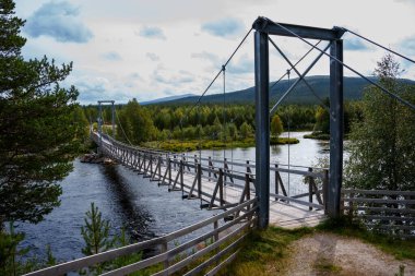 Göz kamaştırıcı ve görkemli bir asma köprüsü zarif bir şekilde yemyeşil bir manzaranın ortasındaki huzurlu bir nehri geçiyor.
