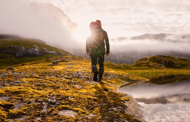 Yalnız bir yürüyüşçü, yumuşak ve sıcak güneş ışığıyla yıkanmış nefes kesici bir dağ manzarasında yol alır.