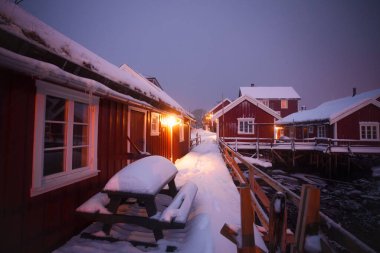 Charming rustic cabins lined up along a snowy path beautifully create a tranquil and serene winter atmosphere clipart