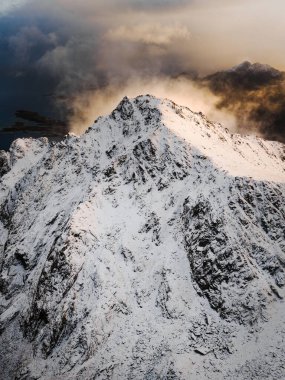 Güneş tarafından güzelce aydınlatılmış, karla kaplı bir dağın nefes kesici ve çarpıcı manzarası.