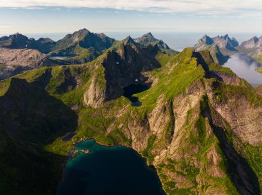Havadan bakıldığında, engebeli dağların, gür, canlı yamaçlarla süslendiği ve aşağıdan yansıtan sakin bir göl görülür.