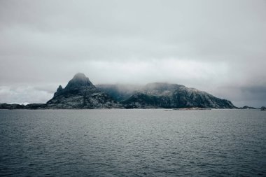 Bu sakin manzara sakin sular ve kasvetli bulutlu gökyüzüyle çevrili sisli, ıssız bir adayı gösteriyor.