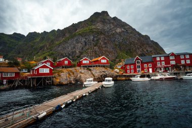 Deniz kenarında büyüleyici bir köy. Resimli kırmızı kulübeleri, görkemli dağları ve güzel bulutlu gökyüzü var.