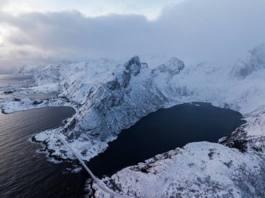 Uçsuz bucaksız bulutlu gökyüzünün altında sakin sularla birlikte karla kaplı dağları gösteren nefes kesici bir manzara.