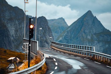 Manzaralı bir manzara, arka planda bir trafik ışığı olan, güzel dağların arasından geçen dolambaçlı bir yolu gösteriyor.