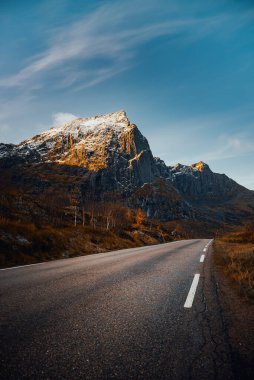 Güzel, dolambaçlı bir yol, canlı mavi gökyüzünün altında nefes kesici dağ manzaraları arasında dolanıyor.
