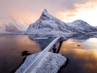 Gün batımında bir köprüyü gösteren nefes kesici güzellikte ve nefes kesici karlı bir dağ manzarası gerçekten büyüleyici.