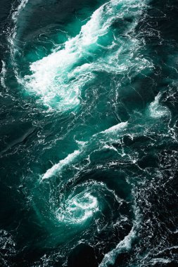 Parlak turkuaz ve koyu tonlarda okyanus sularının büyüleyici hareketlerini gösteren bir hava manzarası.
