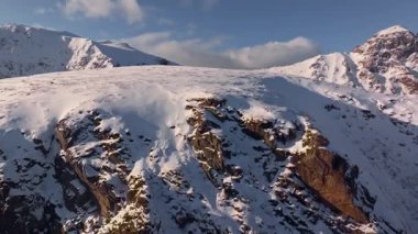 Çarpıcı, karla kaplı dağ zirvelerinin hava manzarası dramatik ve engebeli bir kaya manzarasıyla vurgulanır.