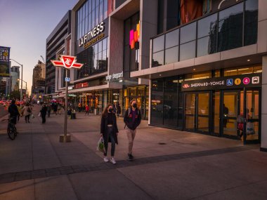 Toronto, Ontario, Canada - 09 23 2022: A young couple walking along Younge Street in front of Sheppard Yonge TTC subway station in North York neighborhood of Toronto city in the evening with last sun