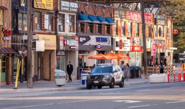 Toronto, Ontario, Canada - 10 03 2022: Toronto olice cruiser parked in front of a row of old two storey buildings with bars, cafes, small strores under various colorfull signs and banners on Younge