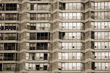 Urban geometry. Rows of large windows with various curtains, shutters, blinds, jalousies in a bricky wall of residential condo high-rise building. Black and white. Monochrome. Sepia.