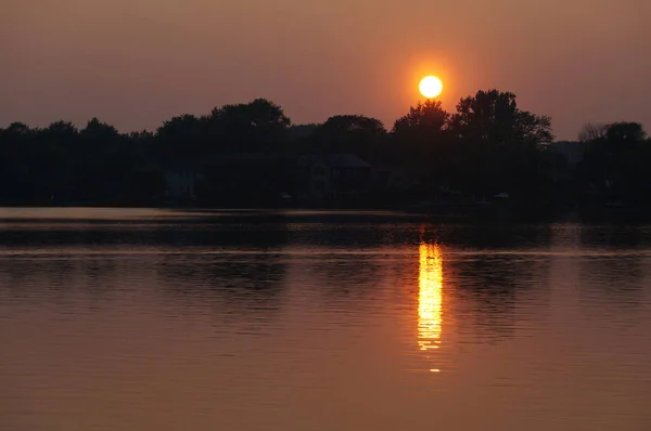 Setting sun overlooks still water of a Lake Wilcox reflecting orange sunset sun rays in Lake Wilcox Park, Richmond Hill, Ontario, Canada.