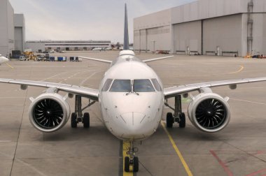 Geniş bir havaalanında, beton pist üzerinde oturan modern bir Twinjet uçağının ön görüntüsü..