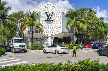 Miami, Florida, ABD - 03: 12: 2024: Sarı yelekli genç bir bayan trafik kontrolörü, LOUIS 'un önünden geçen caddelerin ortasında, Miami Tasarım Bölgesi Mağazası önünde işaret ediyor.