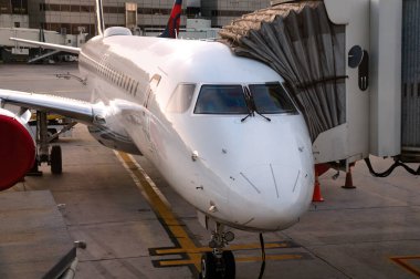 Beyaz, modern, kokpit pencereli bir jet uçağının ön görüntüsü. Uçak beton bir pistin üzerinde duruyor..