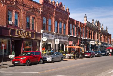 Port Perry, Ontario, Kanada - 2024 10 05: Queen Caddesi boyunca güneşli bir gün manzarası ve çeşitli küçük işletmelerin büyük mağazalarının önüne park edilmiş iki katlı eski tuğla binalar ve arabalar..