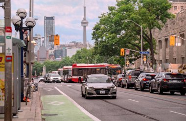 Toronto, Ontario, Kanada - 06: 21 2025: Güneşli yaz gününde Queens Park caddesinde trafik, Savaş Anıtı, Yasama Ofisi binası ve Toronto şehir merkezinin gökdelenleri.