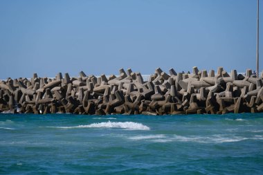 Beton dalga kırıcı tetrapodlar açık mavi gökyüzünün altında kıyı şeridini güçlü deniz dalgalarından koruyor.