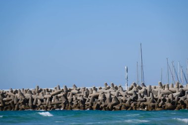 Beton dalga kırıcı tetrapodlar açık mavi gökyüzünün altında kıyı şeridini güçlü deniz dalgalarından koruyor..