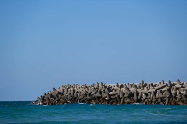 Beton dalga kırıcı tetrapodlar açık mavi gökyüzünün altında kıyı şeridini güçlü deniz dalgalarından koruyor..