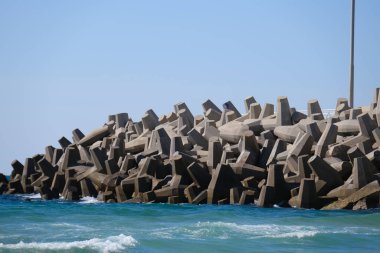 Beton dalga kırıcı tetrapodlar açık mavi gökyüzünün altında kıyı şeridini güçlü deniz dalgalarından koruyor..