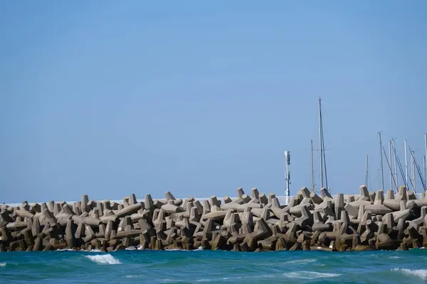 Beton dalga kırıcı tetrapodlar açık mavi gökyüzünün altında kıyı şeridini güçlü deniz dalgalarından koruyor..