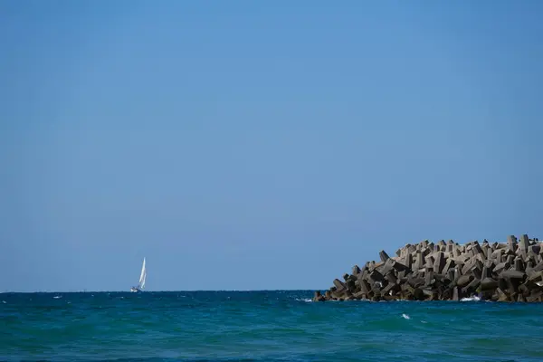Beton dalga kırıcı tetrapodlar açık mavi gökyüzünün altında kıyı şeridini güçlü deniz dalgalarından koruyor..