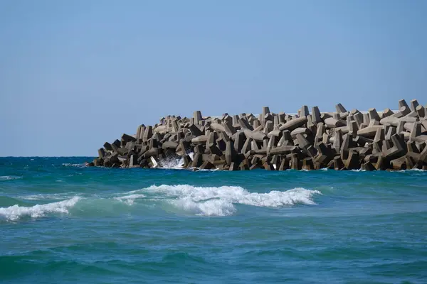 Beton dalga kırıcı tetrapodlar açık mavi gökyüzünün altında kıyı şeridini güçlü deniz dalgalarından koruyor..