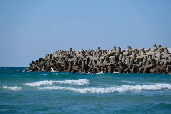 Beton dalga kırıcı tetrapodlar açık mavi gökyüzünün altında kıyı şeridini güçlü deniz dalgalarından koruyor..