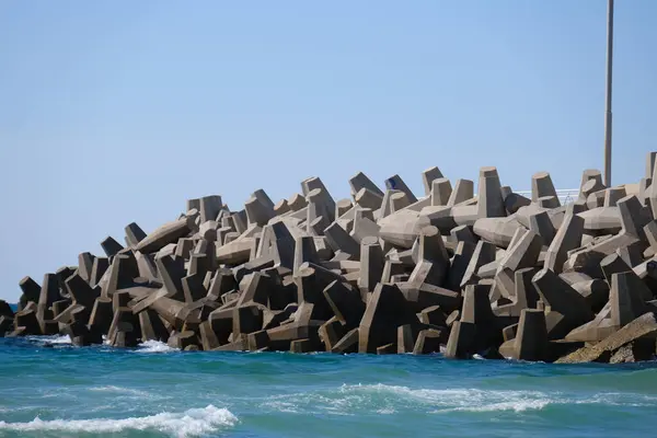 Beton dalga kırıcı tetrapodlar açık mavi gökyüzünün altında kıyı şeridini güçlü deniz dalgalarından koruyor..