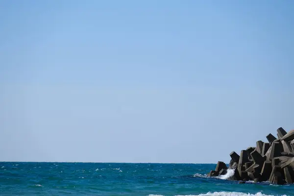 Beton dalga kırıcı tetrapodlar açık mavi gökyüzünün altında kıyı şeridini güçlü deniz dalgalarından koruyor..