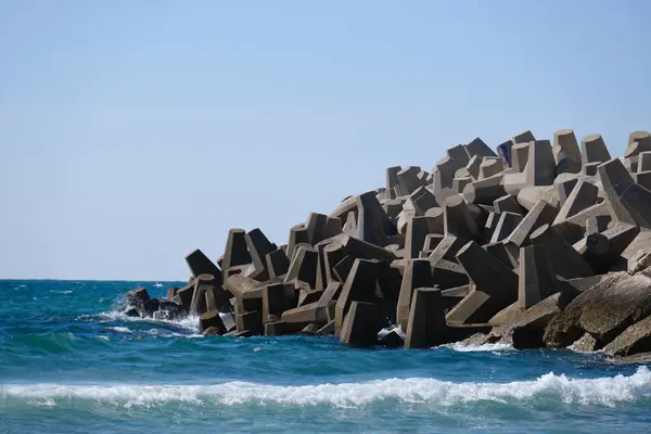 Beton dalga kırıcı tetrapodlar açık mavi gökyüzünün altında kıyı şeridini güçlü deniz dalgalarından koruyor..