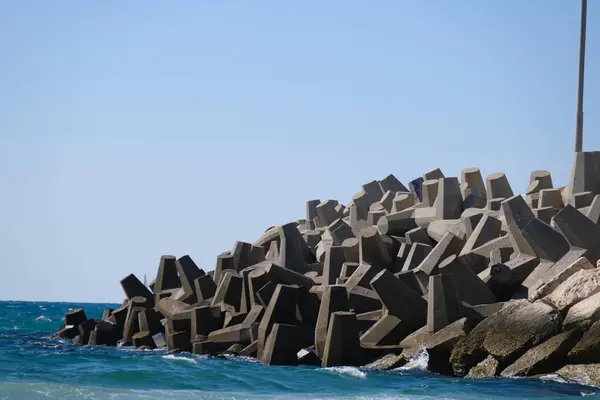 Beton dalga kırıcı tetrapodlar açık mavi gökyüzünün altında kıyı şeridini güçlü deniz dalgalarından koruyor..