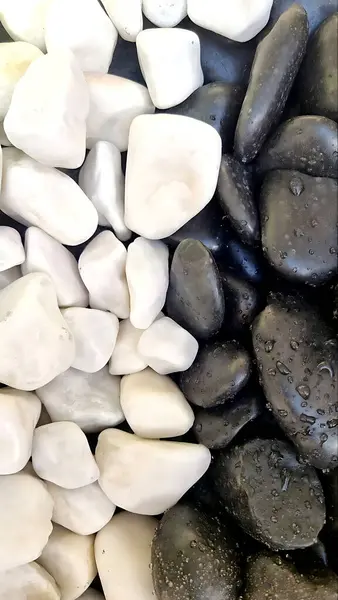 Siyah ve beyaz çakıl taşlarının zıtlaşması ve koyu taşların üzerine su damlacıkları. Kompozisyon dokuyu, dengeyi ve minimalizmi vurguluyor.