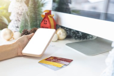 Nazik eller akıllı telefonu, boş ekranı, şenlik sahnesini, kredi kartlarıyla süslenmiş güzel bir Noel ağacını, Noel toplarını, çam kozalaklarını ve kırmızı ev hediye paketini beşiğine bağlar..