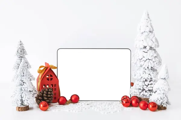 Tapelet with a white screen mock-up and White calendar with a festive scene of a beautiful Christmas tree adorned, with Christmas balls, pine cones, and a red house gift box.